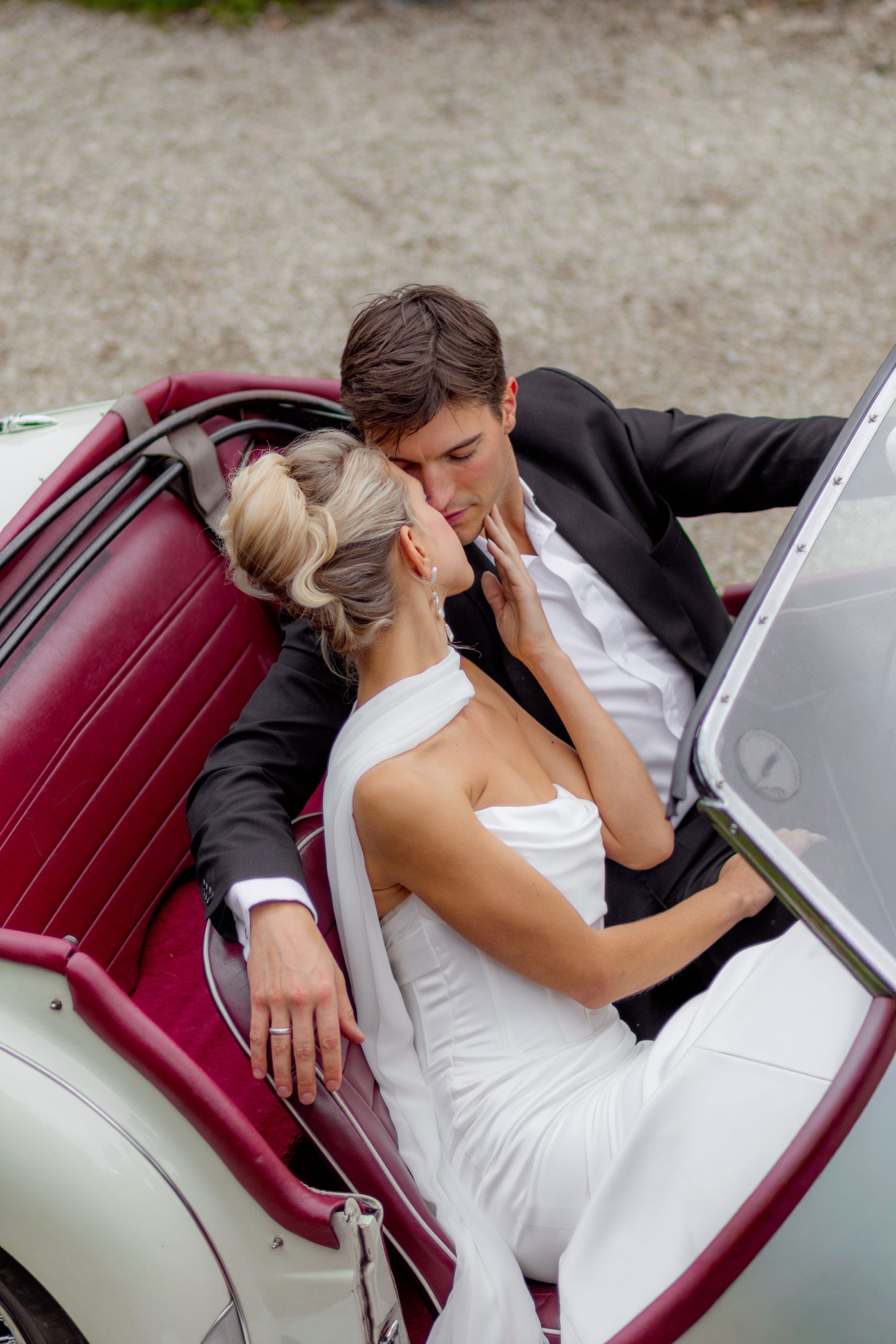 Couple élégant sur le point de s’embrasser dans une voiture vintage décapotable blanche Triumph, mariage chic en France